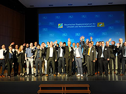 Eine große Gruppe von Personen (die Mitarbeitenden und Partnerinnen sowie Partner im Projektverbund ForCYCLE II) steht winkend auf einer Bühne, darunter Staatsminister Thorsten Glauber in der Mitte. Bildquelle: StMUV Eine große Gruppe von Personen (die Mitarbeitenden und Partnerinnen sowie Partner im Projektverbund ForCYCLE II) steht winkend auf einer Bühne, darunter Staatsminister Thorsten Glauber in der Mitte. Bildquelle: StMUV